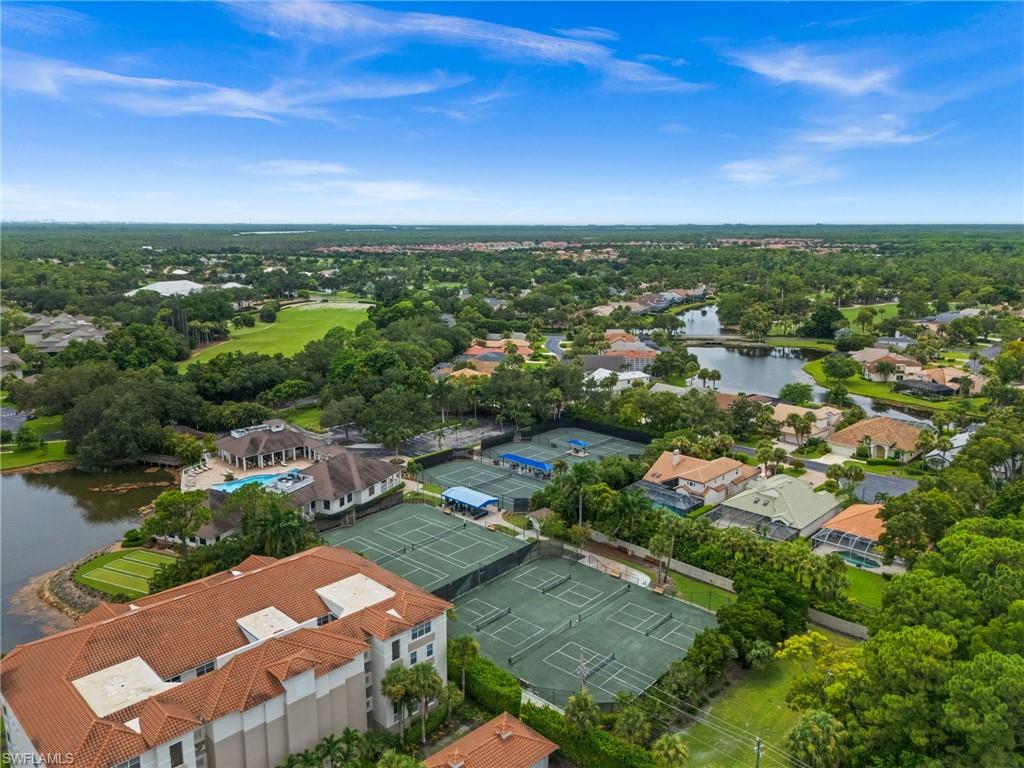 Lush landscaping with mature trees, multiple tennis courts, extensive water features, resort-style pool, and a building with a terra cotta tile roof