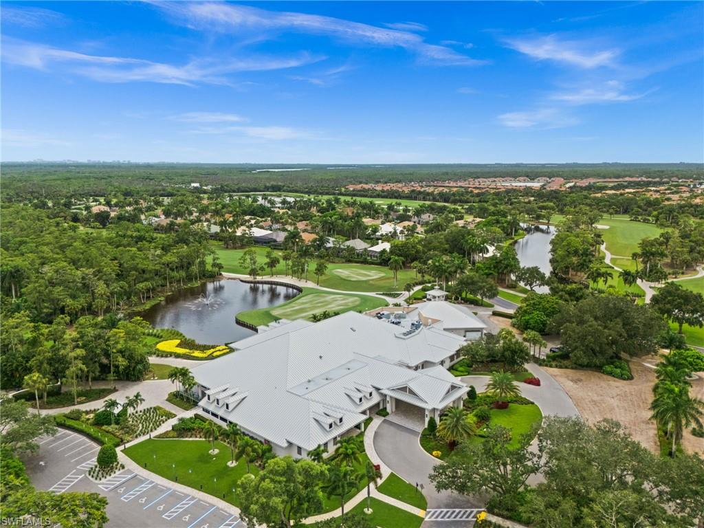 Clubhouse structure with white siding and gray roofing, surrounded by lush landscaping, a paved parking area, and an adjacent golf course with water features