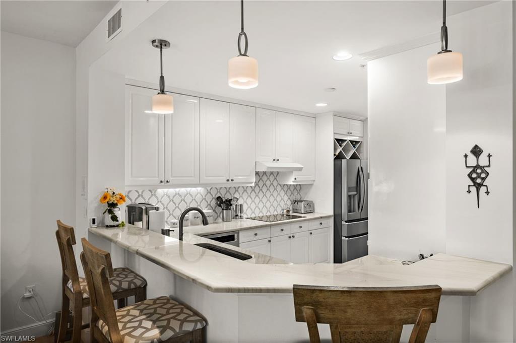 Kitchen featuring white cabinetry, light-toned countertops, a patterned tile backsplash, stainless steel appliances, and pendant lighting