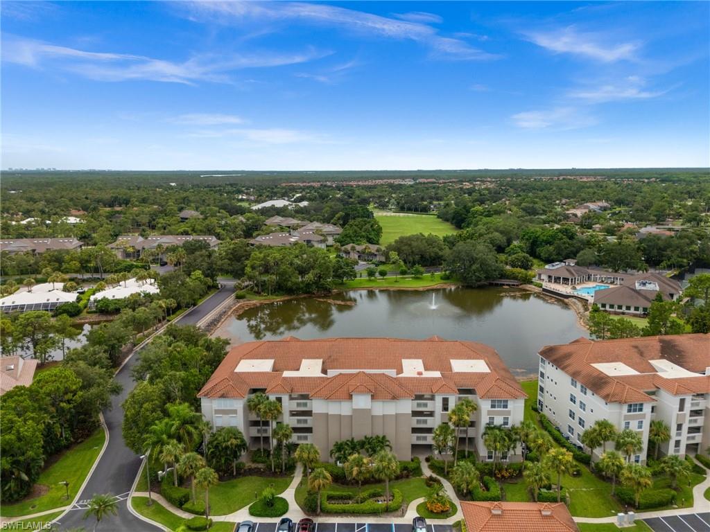 Multi-story building featuring a tile roof, surrounded by mature landscaping, a pond with a fountain, and a paved parking area