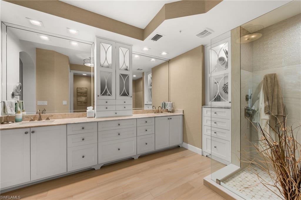 Dual vanity with undermount sinks, expansive mirrors, wood-finish flooring, and a glass-enclosed shower