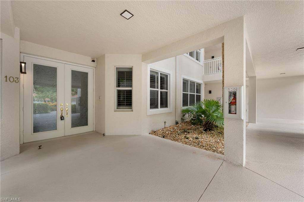 Double glass entry doors, exterior wall sconce, recessed ceiling lighting, louvered window shutters, and a courtyard planting bed