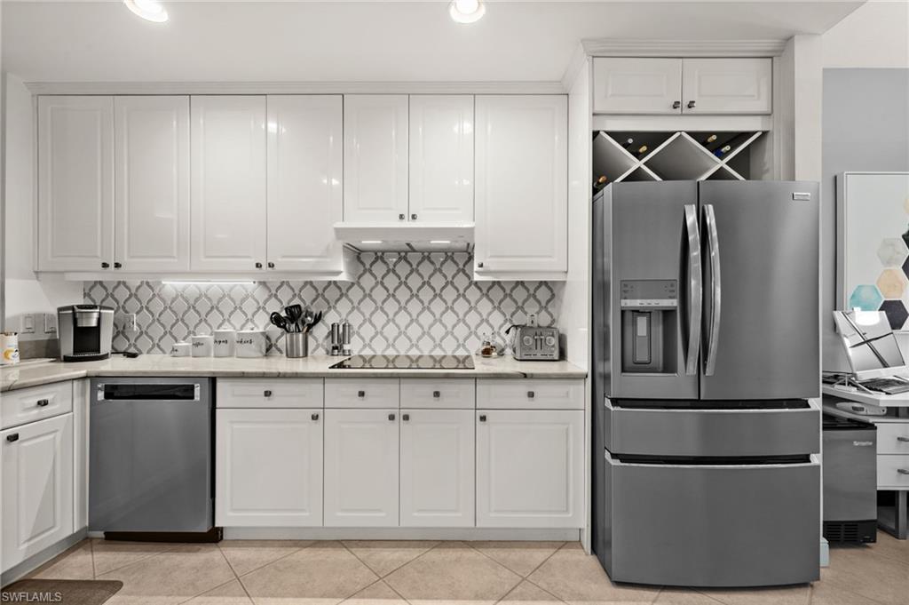 White cabinetry, stainless steel appliances, patterned tile backsplash, recessed lighting, and built-in wine storage