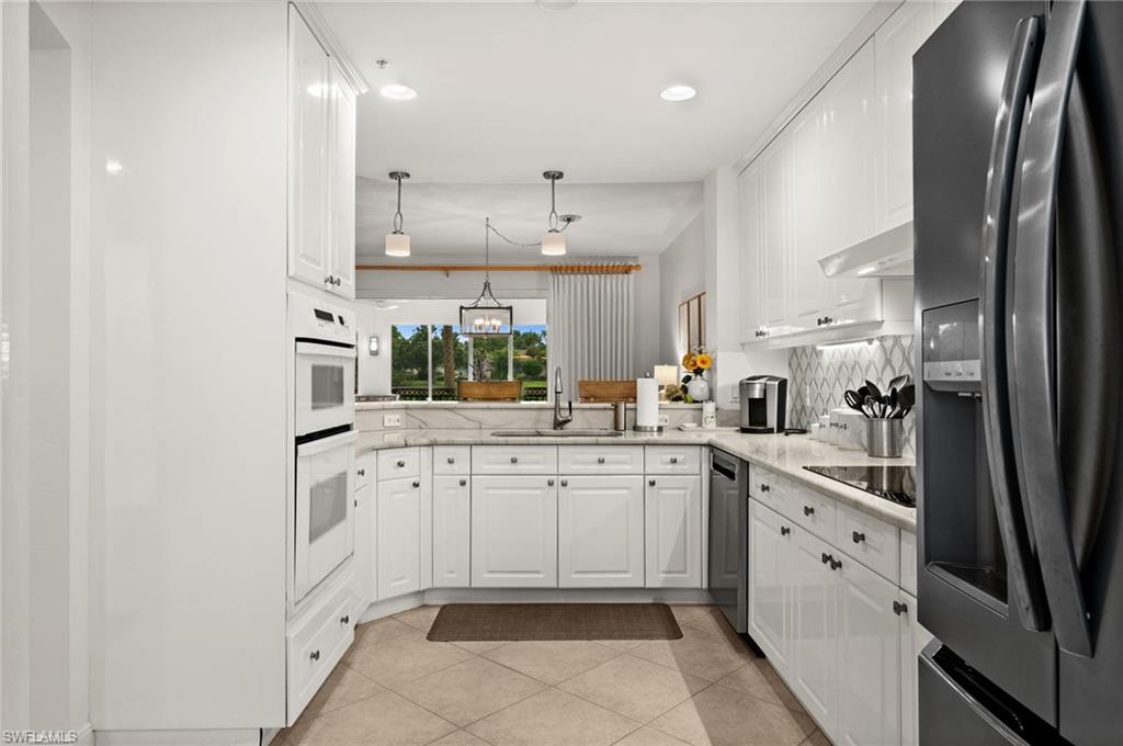 White cabinetry with dark hardware, built-in double ovens, light-toned tile flooring, and a patterned backsplash