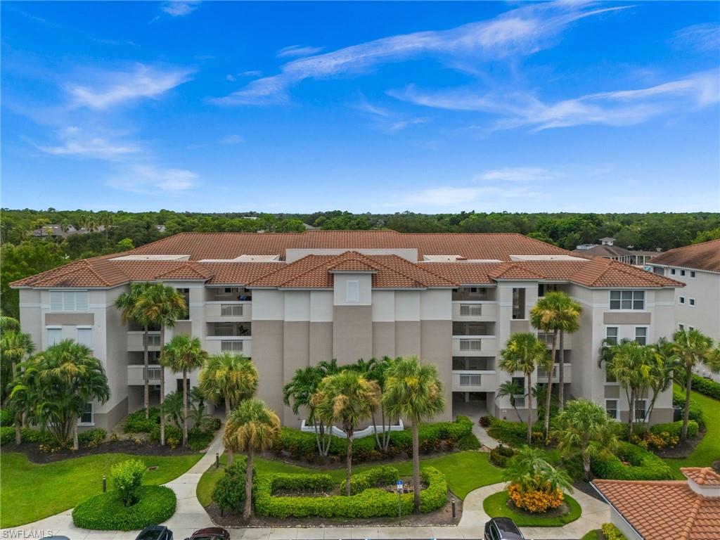 Multi-story building featuring a tile roof, multiple balconies, mature palm trees, and manicured landscaping