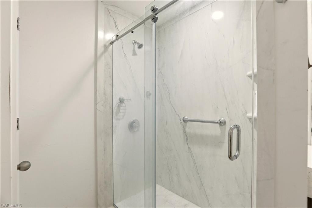 Glass-enclosed shower with a sliding door, marble-patterned wall panels, a built-in shower niche, and polished chrome fixtures