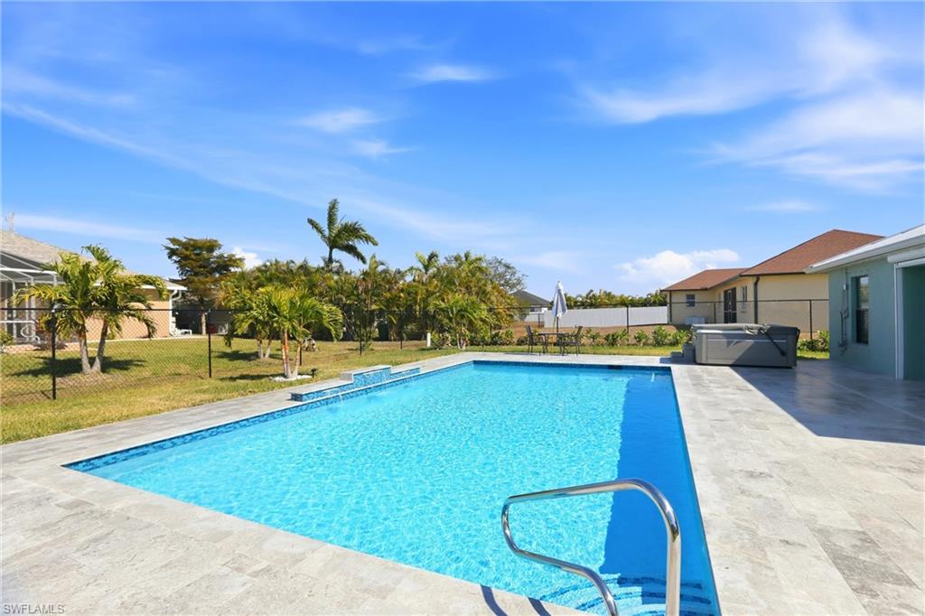 Rectangular swimming pool with integrated steps, surrounded by light-toned patio pavers and a manicured lawn