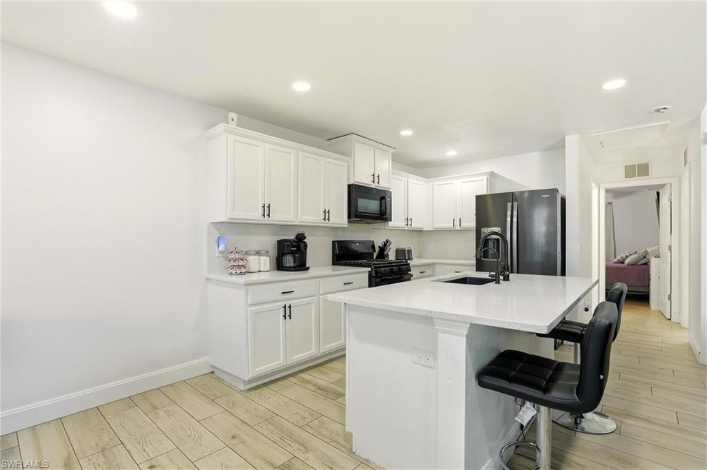 Kitchen featuring white cabinetry, light-toned wood-finish flooring, recessed lighting, and a kitchen island with a dark sink and matte black faucet