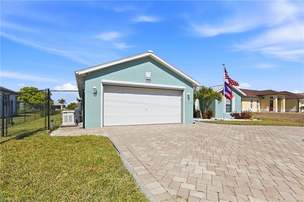 Stucco exterior with a two-car garage, paver driveway, chain-link fencing, and mature landscaping