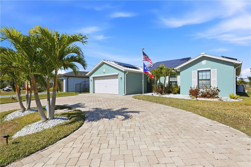 Paver driveway, mature palm trees, solar panels, attached garage, and white decorative shutters