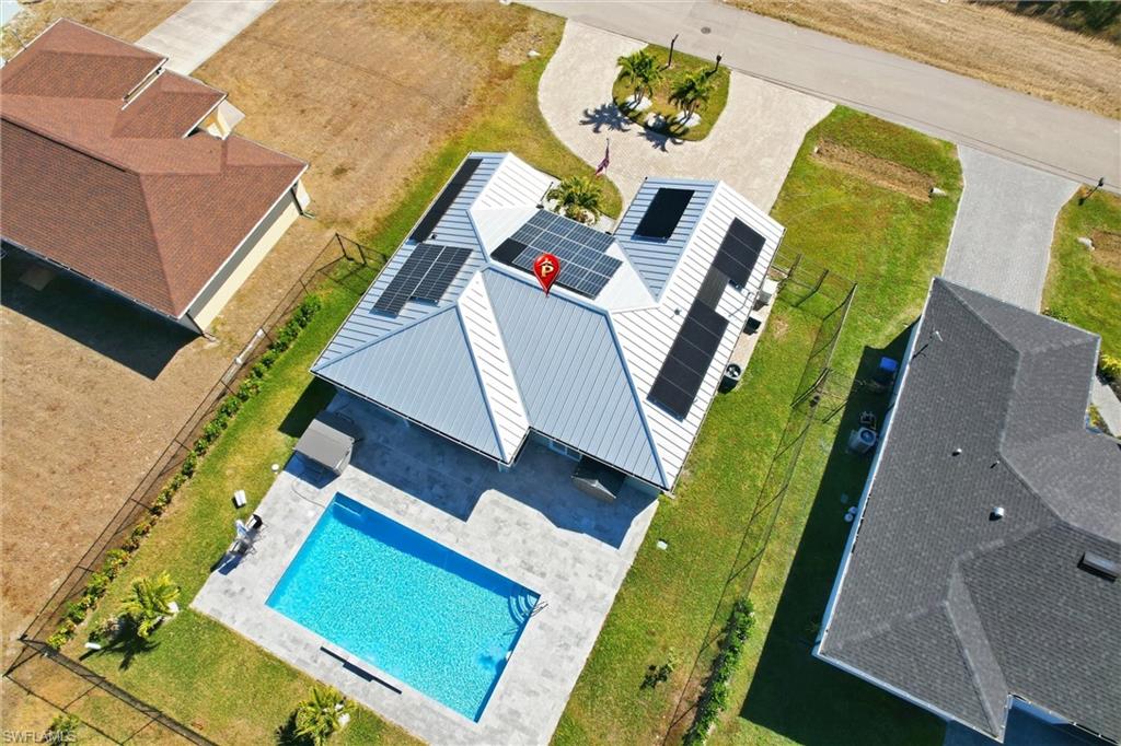 Metal roof with integrated solar panels, rectangular swimming pool, paver pool deck, and fenced backyard