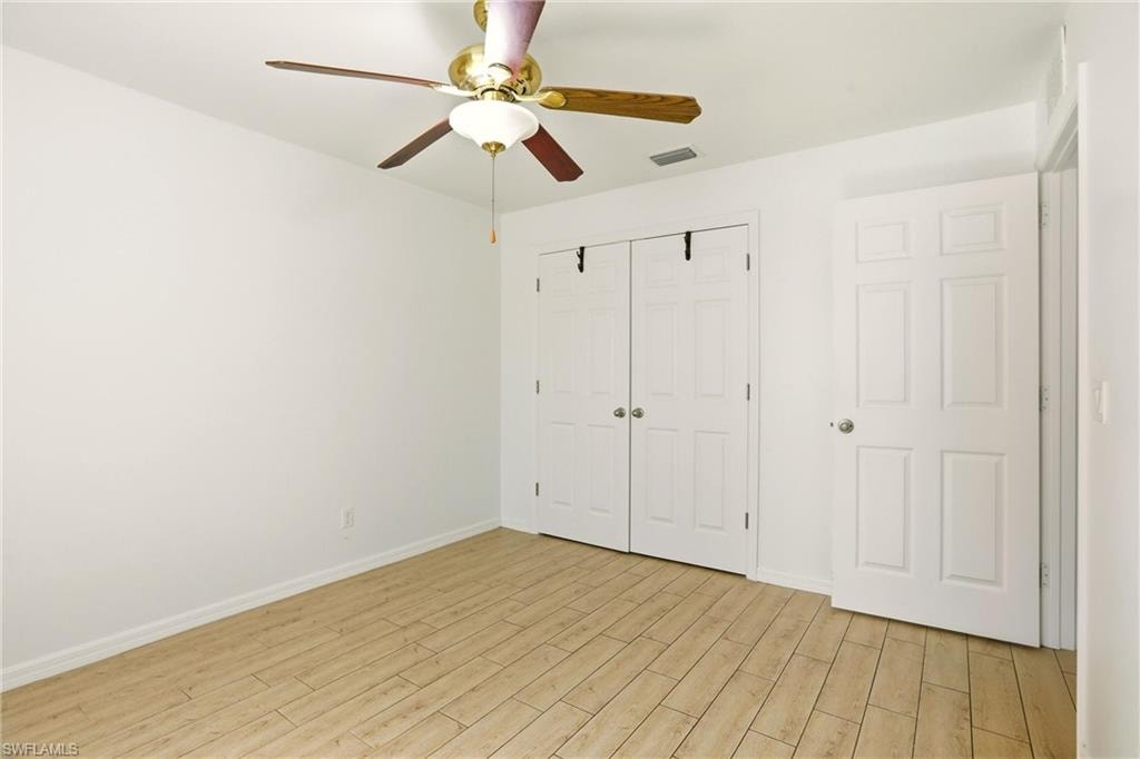 Light wood-finish flooring, white walls, ceiling fan with light fixture, white paneled doors