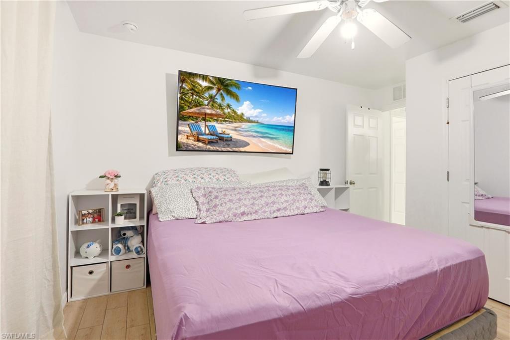 White painted walls, wood-finish flooring, ceiling fan with light fixture, white interior door, and built-in closet with mirror