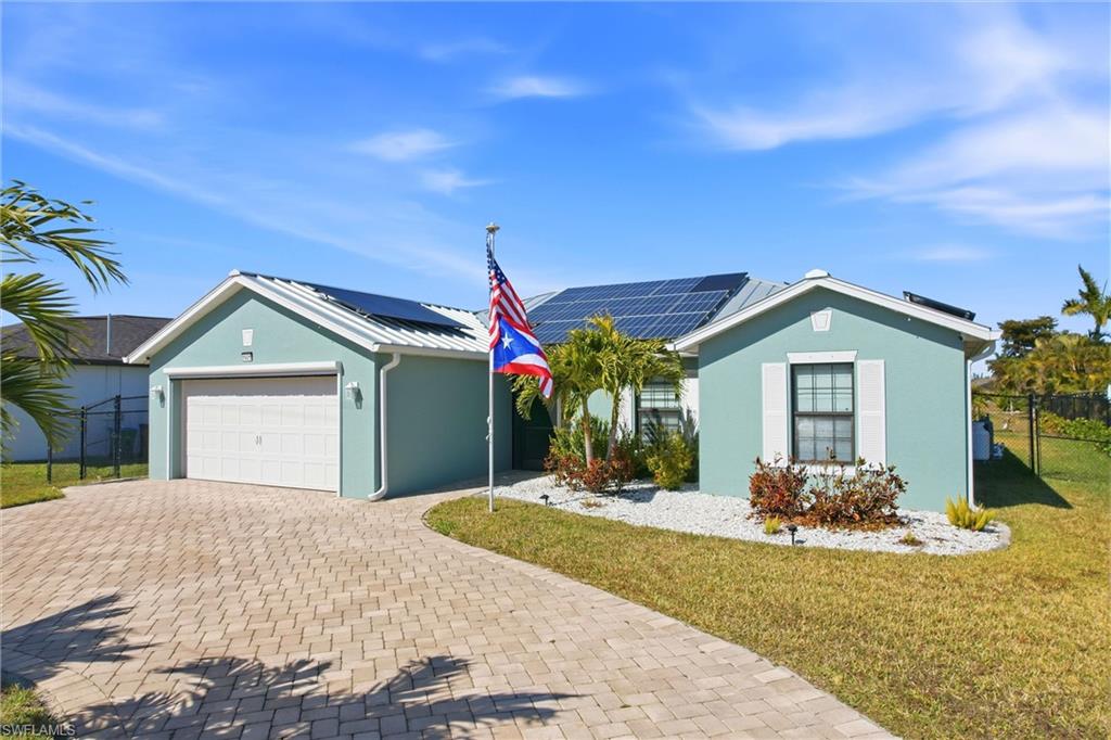 Stucco exterior with white trim, solar panels, a paver driveway, and an attached garage
