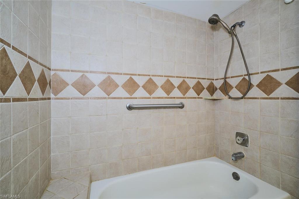 Bathtub with a tiled surround featuring a decorative diamond pattern, a handheld shower fixture, and a wall-mounted grab bar