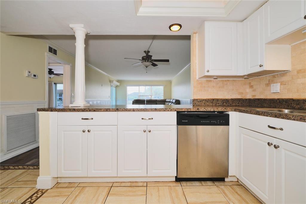 White cabinetry with stainless steel dishwasher, brown speckled countertops, and tile backsplash