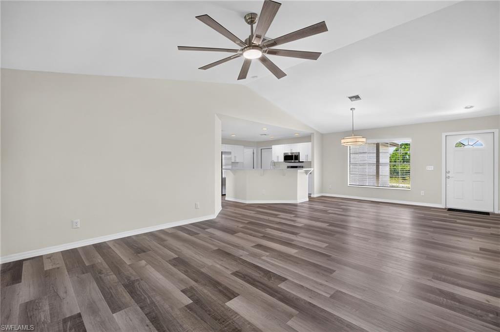 Vaulted ceiling with a ceiling fan, wood-finish flooring, white entry door with an arched window insert, and a pendant light fixture