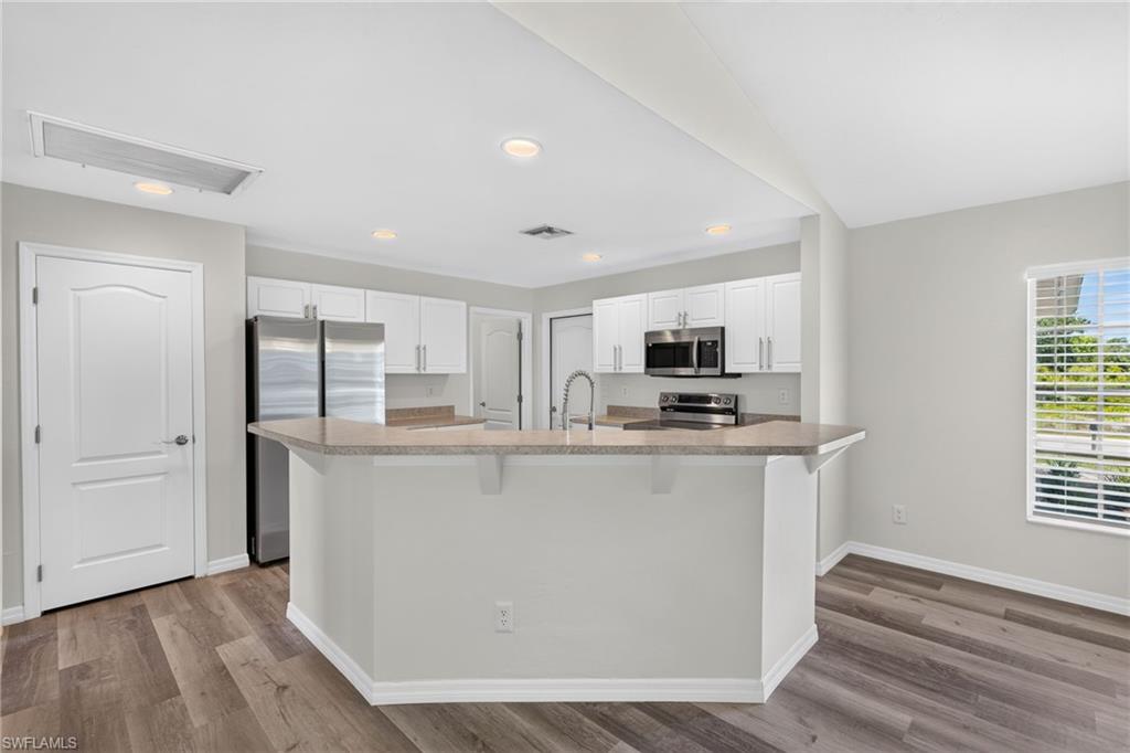Kitchen featuring white cabinetry, stainless steel appliances, a breakfast bar, recessed lighting, and wood-finish flooring