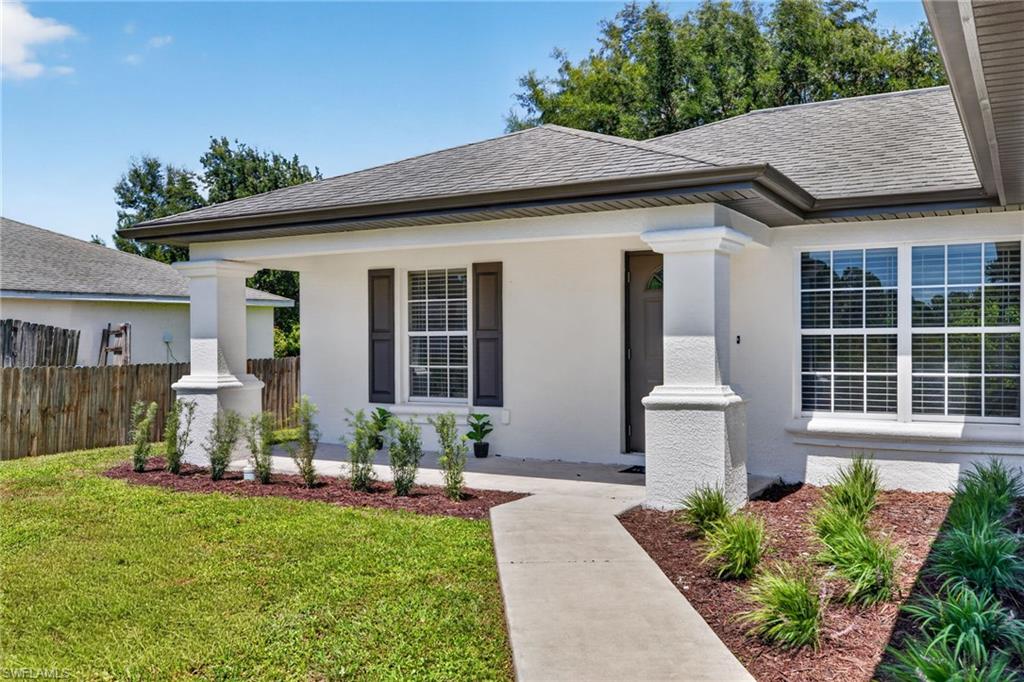 Stucco exterior with a covered entry, white window frames, dark shutters, and a concrete walkway