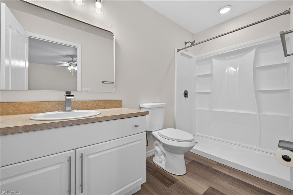 Contemporary bathroom featuring a white vanity with an undermount sink, a warm-toned countertop, a full-width mirror, a white shower and tub combination, and wood-finish flooring