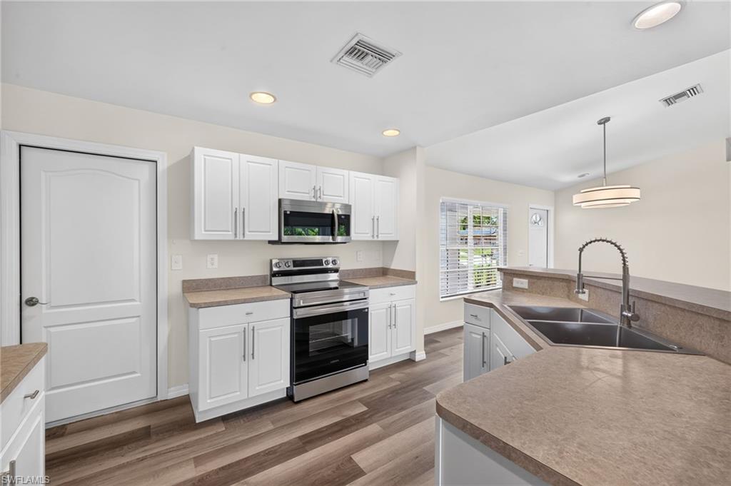 Kitchen featuring stainless steel appliances, white cabinetry, wood-finish flooring, recessed lighting, and a double basin sink with a gooseneck faucet