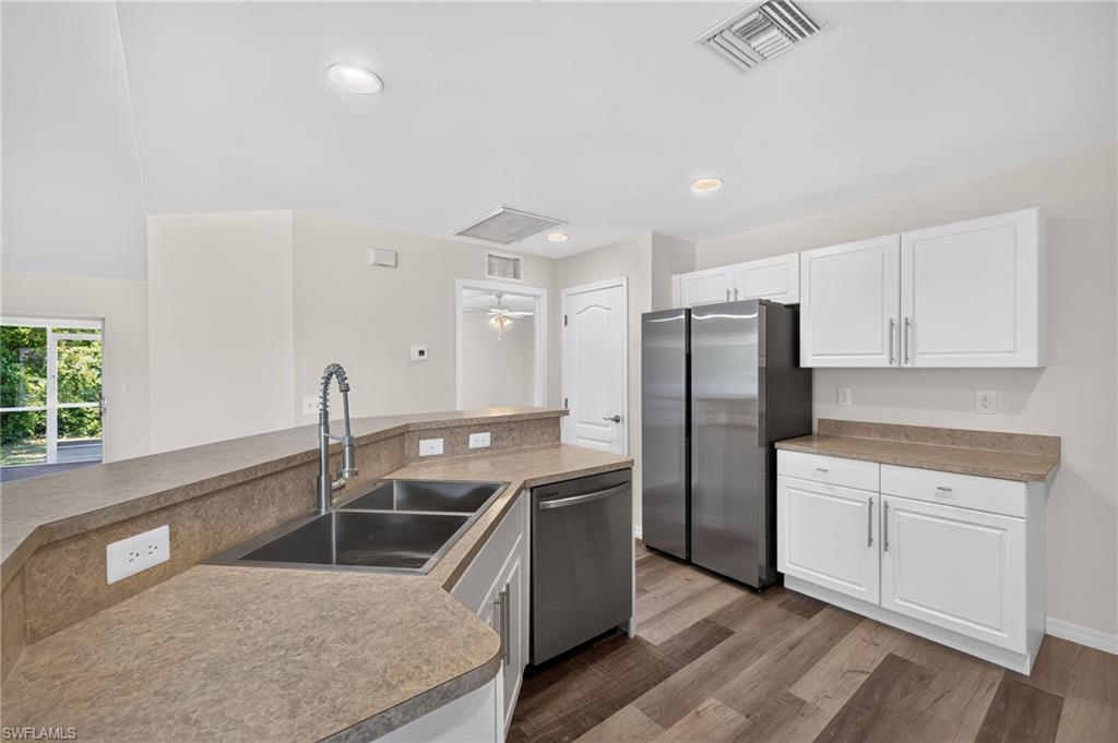 Kitchen featuring wood-finish flooring, stainless steel appliances, white cabinetry, a double basin sink with a high-arc faucet, and countertop space