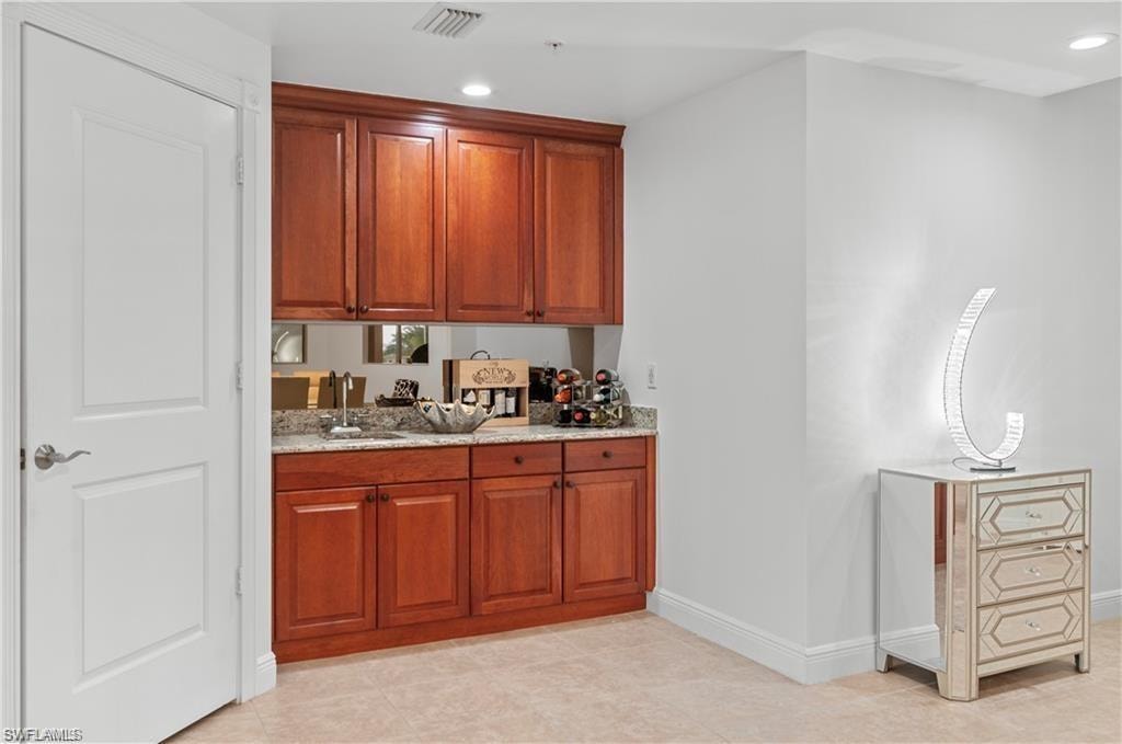 Bar area with recessed lighting, light stone counters, and brown cabinets
