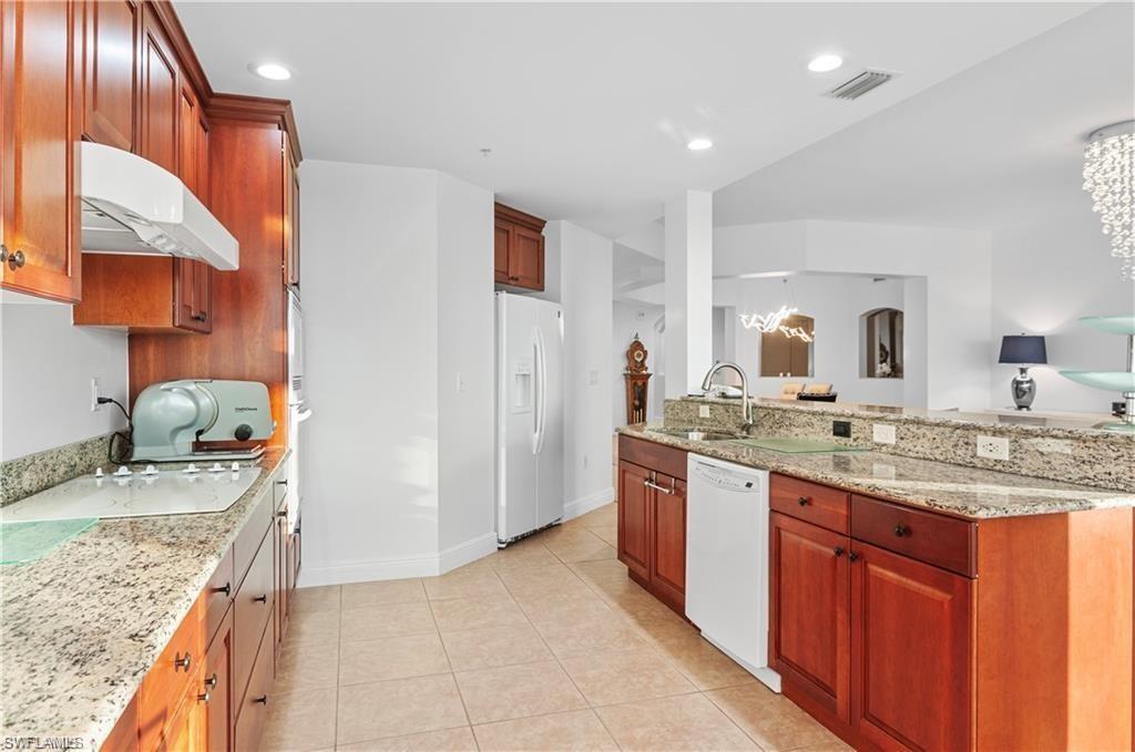Kitchen with light stone counters, light tile patterned floors, white appliances, under cabinet range hood, and brown cabinetry