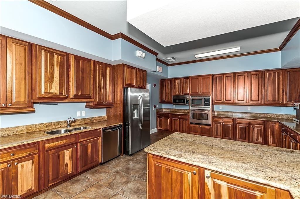 Kitchen featuring crown molding, light stone countertops, appliances with stainless steel finishes, brown cabinetry, and a peninsula