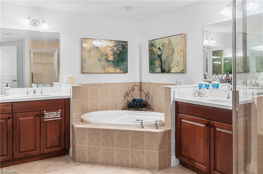 Full bath featuring two vanities, a stall shower, light tile patterned floors, and a bath