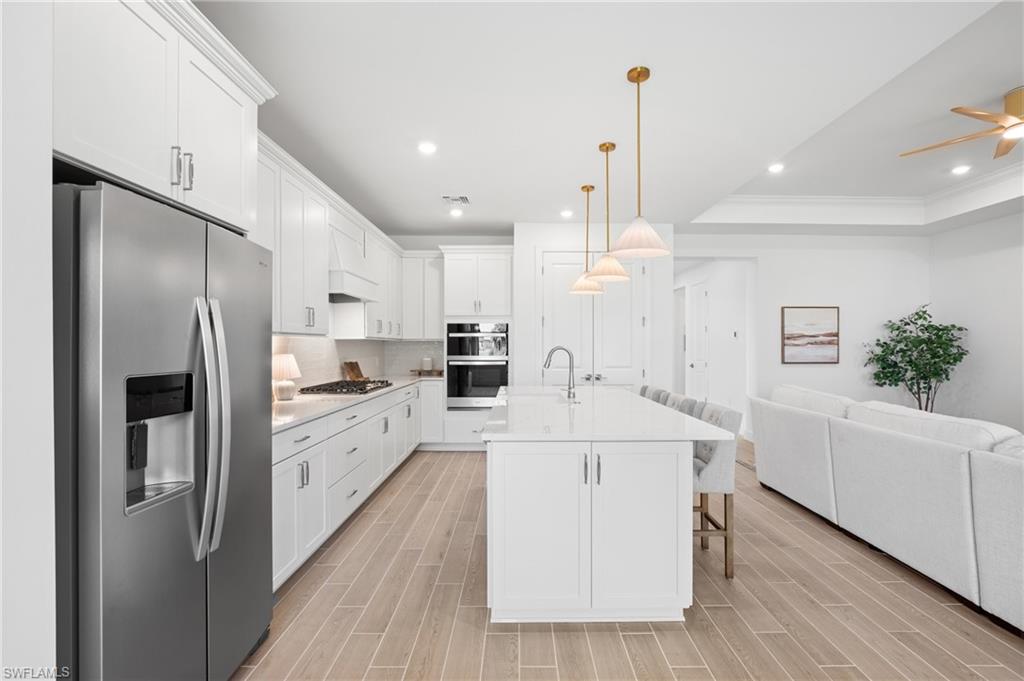 Modern kitchen featuring white cabinetry, stainless steel appliances, a center island with seating, pendant lighting, and wood-finish flooring