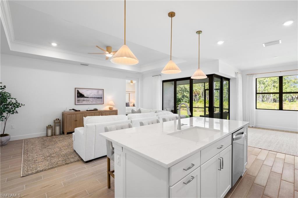 Spacious open-concept interior featuring light tile flooring, a kitchen island with integrated sink, recessed lighting, and large windows