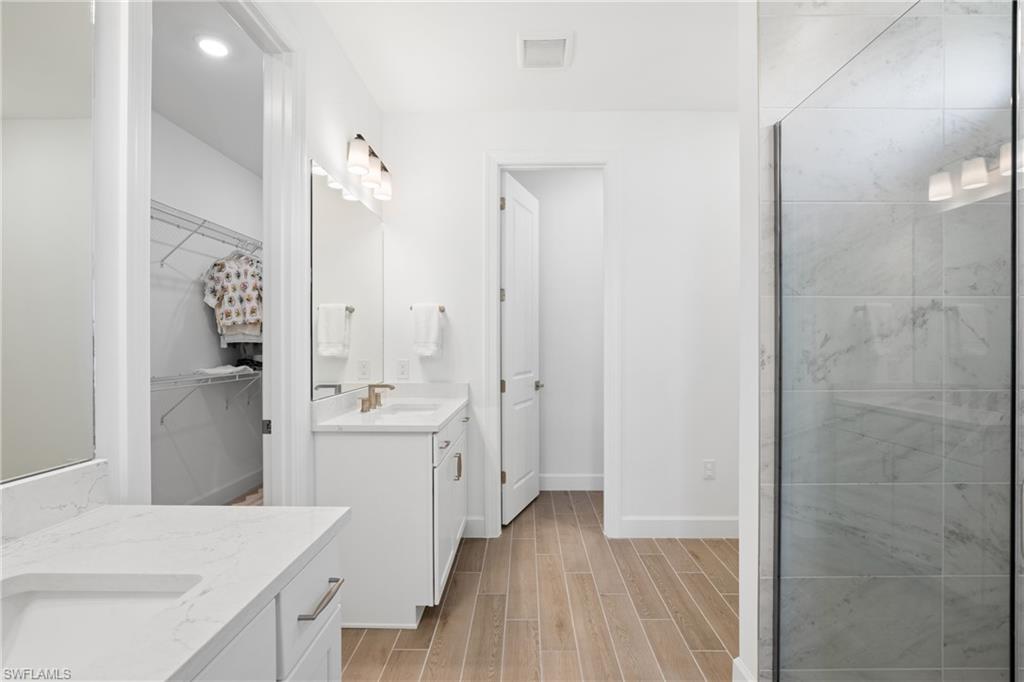 Dual vanity with white cabinetry and integrated sinks, glass-enclosed shower with tile surround, and wood-look flooring