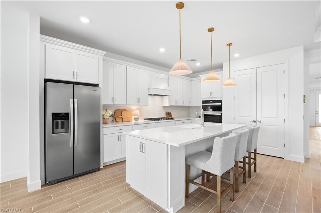 Kitchen featuring an island with seating, white cabinetry, stainless steel appliances, and wood-finish flooring