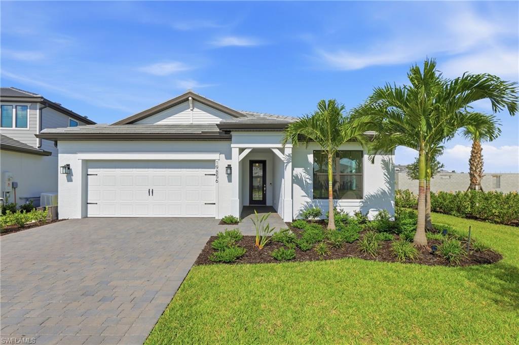 Contemporary single-story residence featuring a two-car garage, paver driveway, and manicured landscaping with mature palm trees