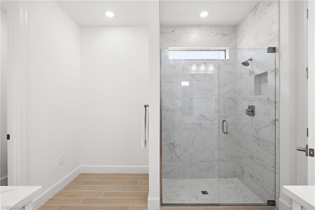 Glass-enclosed shower with marble-finish tile, recessed niche, and a transom window