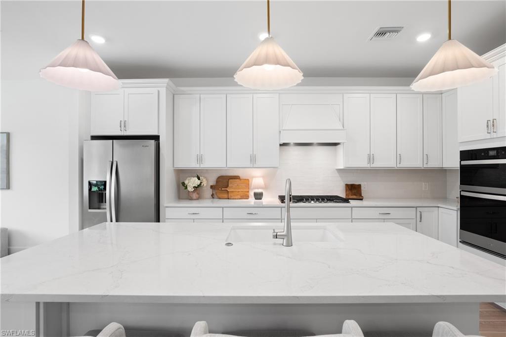 White cabinetry, stainless steel appliances, white subway tile backsplash, white countertop, and contemporary pendant lighting
