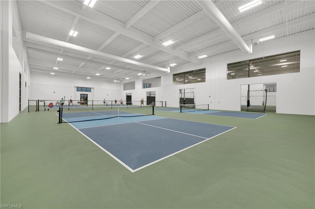 Indoor athletic court with multiple playing surfaces, high ceilings, large perimeter windows, and overhead lighting