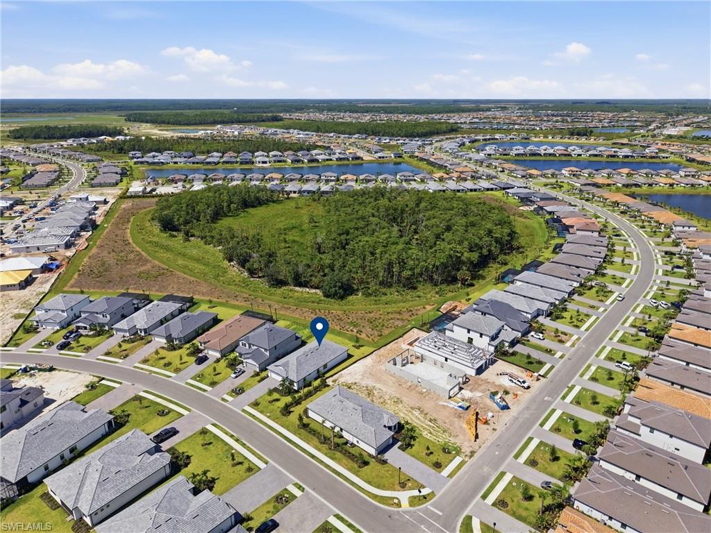 Aerial perspective showcasing a residential development with numerous single-story homes, an unpaved lot with a foundation, and a curved paved street with sidewalks