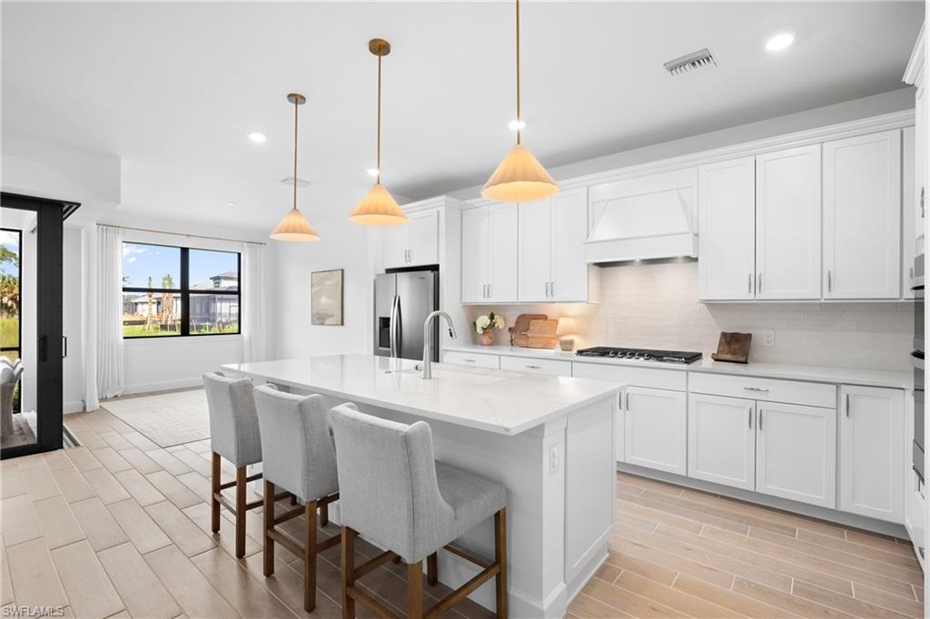 Spacious kitchen with white cabinetry, stainless steel appliances, a center island with pendant lighting, and tile flooring