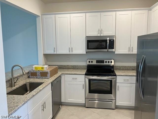 Kitchen featuring light tile patterned floors, white cabinets, stainless steel appliances, and sink