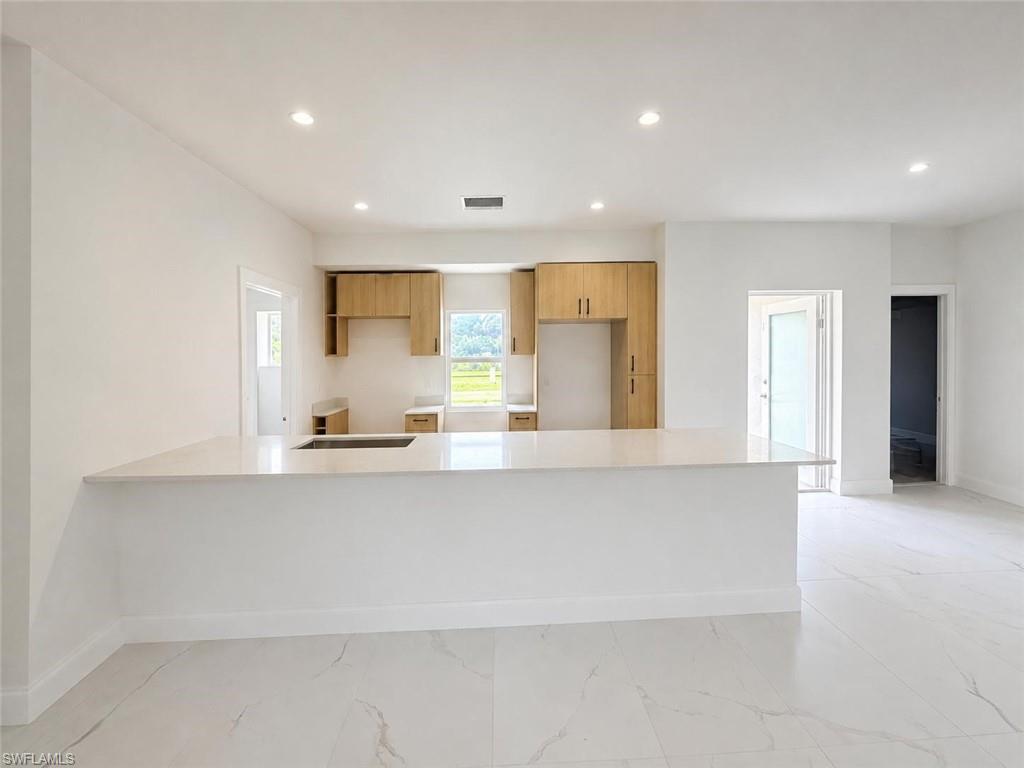 Expansive kitchen island with a light-toned countertop, recessed lighting, wood-finish cabinetry, and large format floor tiling