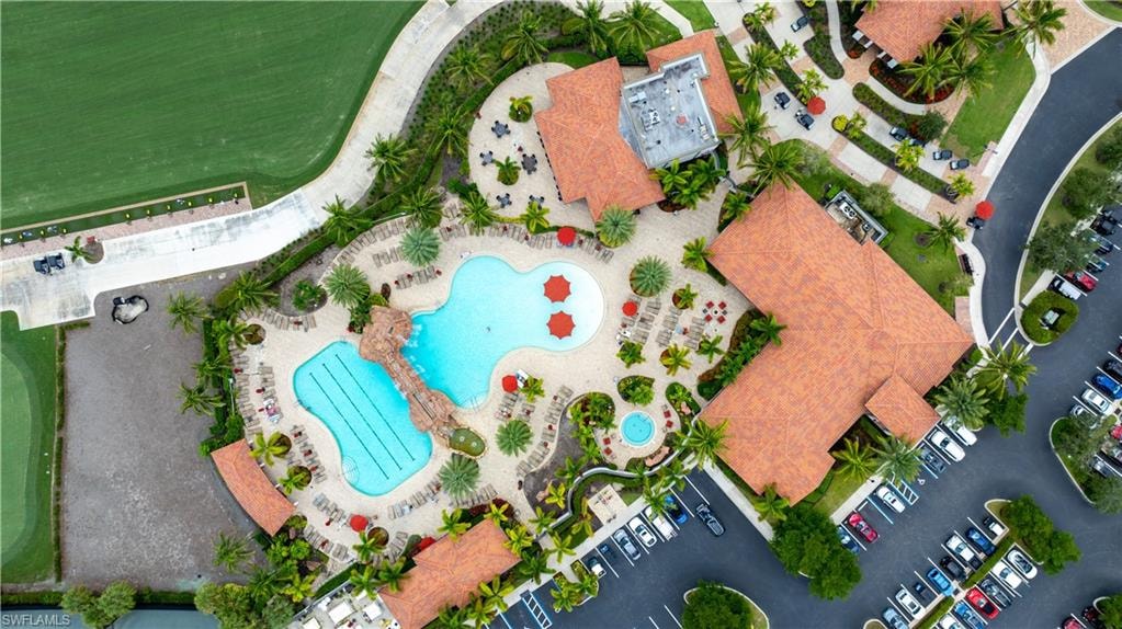 Community amenity complex featuring dual swimming pools, a central building with a terracotta-style roof, multiple parking areas, and mature landscaping