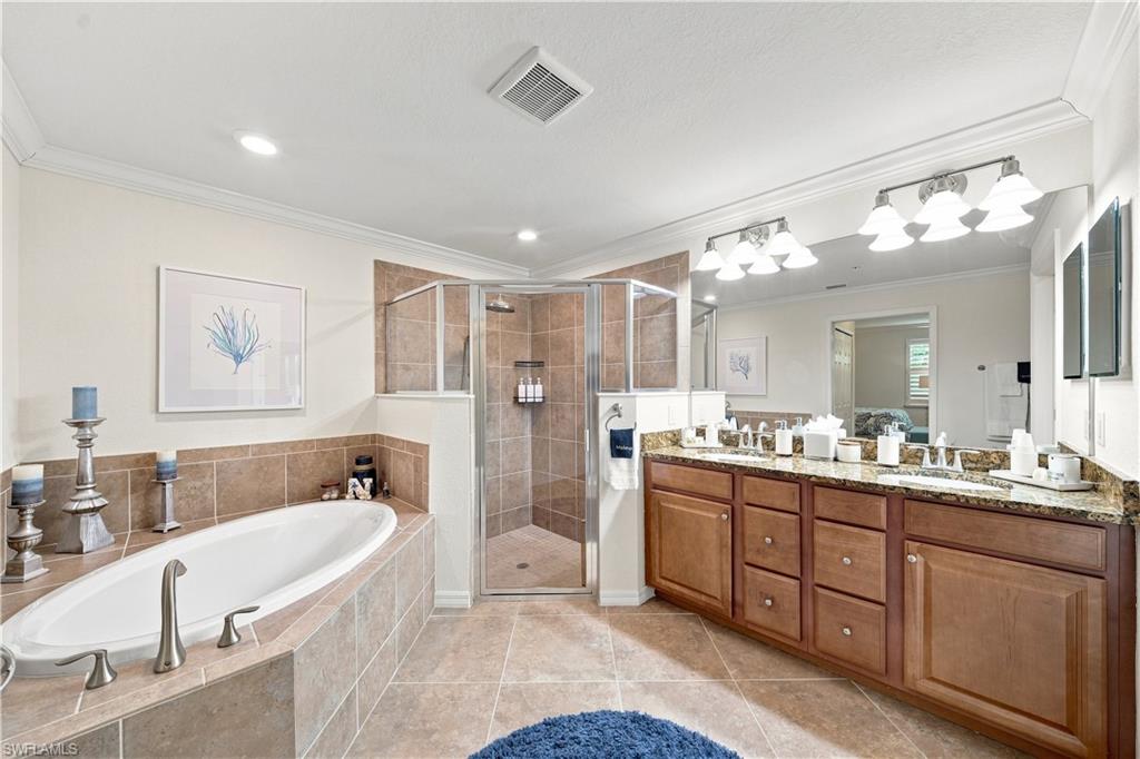 Tiled walk-in shower with glass enclosure, separate soaking tub, expansive double vanity with granite countertop, wood-finish cabinetry, and tiled flooring
