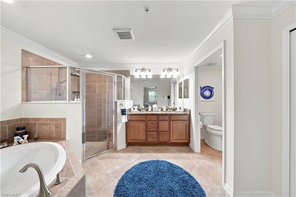 Dual vanity with dark wood-finish cabinetry, tile flooring, glass-enclosed shower, and built-in soaking tub