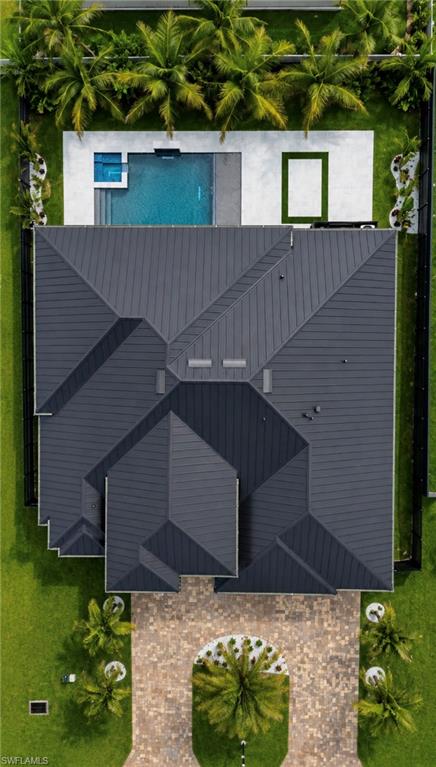 Pitched metal roof system, paver driveway, manicured lawn, rectangular swimming pool, and lush perimeter landscaping