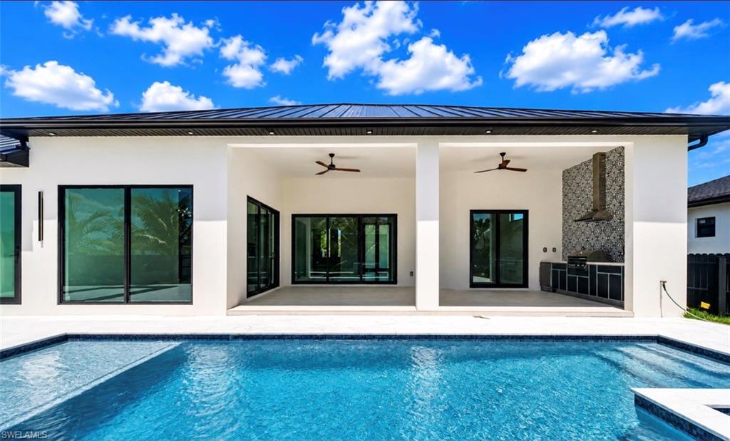 Modern exterior featuring a dark metal roof, clean white stucco finish, and an integrated outdoor kitchen with tile backsplash