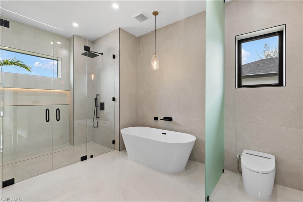 Spacious bath with frameless glass shower enclosure, freestanding soaking tub, and contemporary pendant lighting