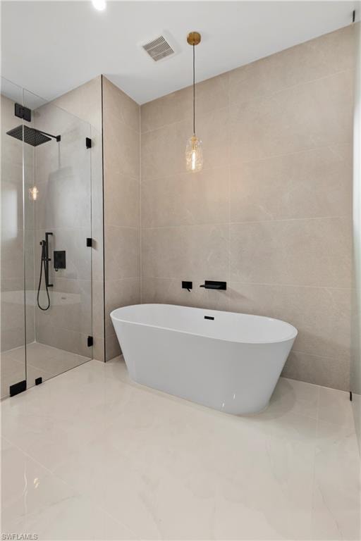 Freestanding soaking tub, floor-to-ceiling tile walls, glass-enclosed shower, matte black fixtures, and a decorative pendant light