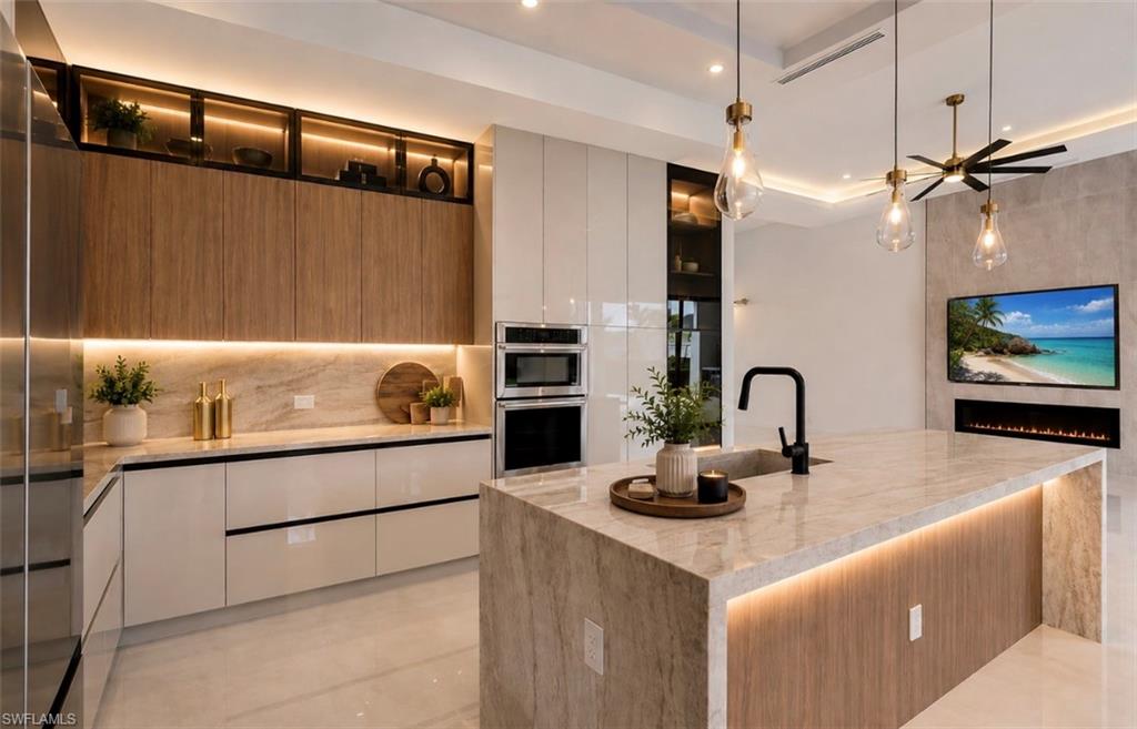 Gourmet kitchen with sleek cabinetry, integrated appliances, a large center island with a built-in sink, and a mounted media display with a linear electric fireplace